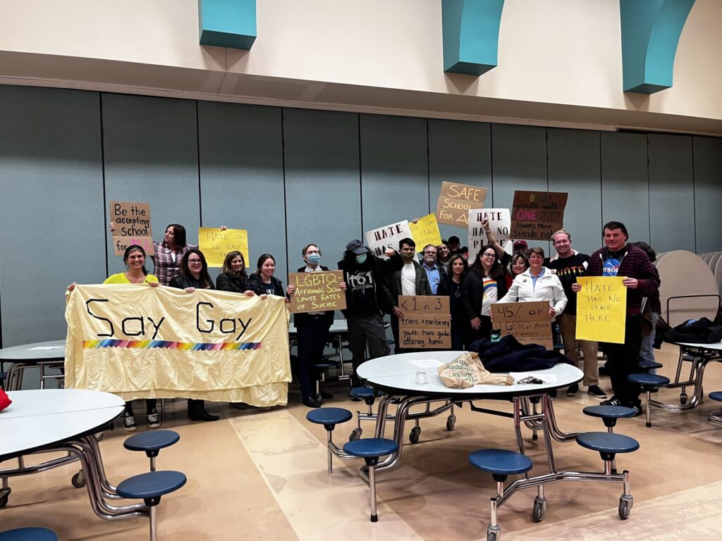 New Jersey advocates hold up signs of support and with facts strewn across them at a school board meeting where transgender student guidance has been contested