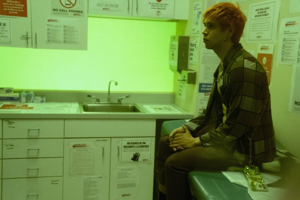 Young ,am with orange hair sitting on a exam table at a doctor's office, lit by a neon green light